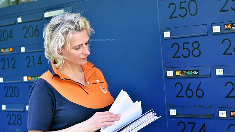 Vrouwelijke postbezorger die post in brievenbus doet