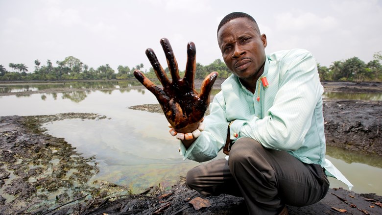 Man (Eric Dooh) houdt hand met olie naar camera in verlaten door olie besmeurde Nigerdelta foto: Marten van Dijl/Milieudefensie