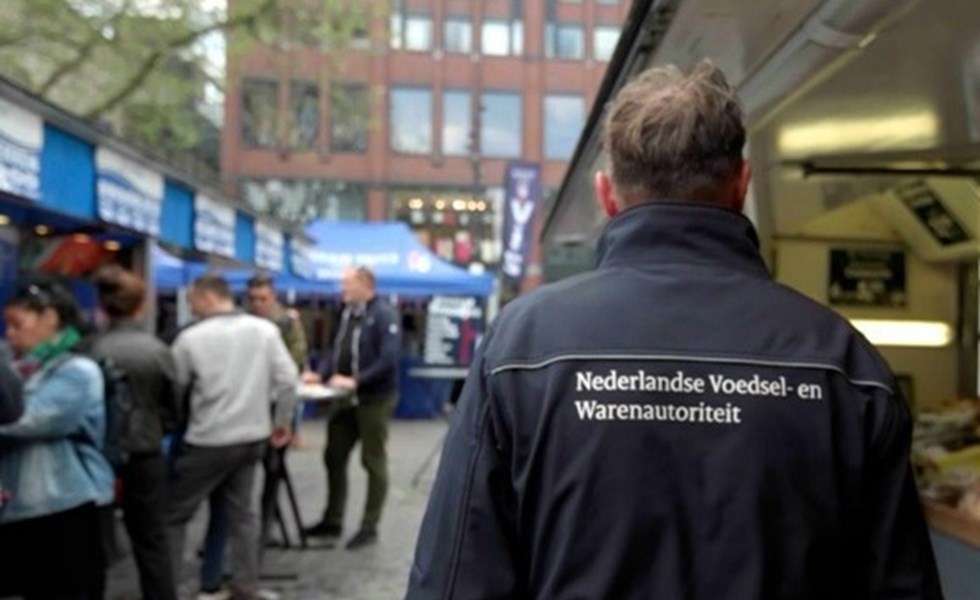 Een man van de Nederlandse Voedsel- en Warenautoriteit loopt over de markt.
