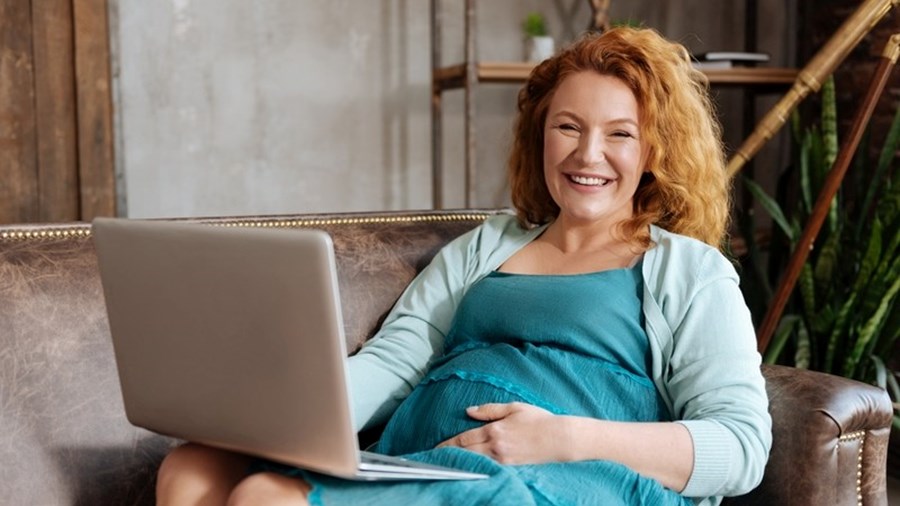 Zwangere vrouw op bank achter laptop